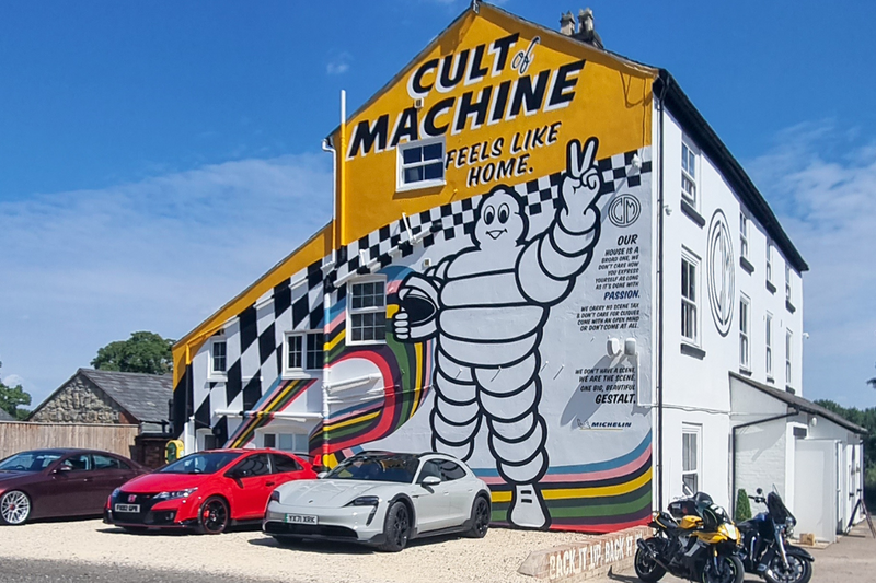 image of vehicles parked outside Caffeine and Machine building decorated with "Cult of Machine" mural